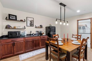 A modern kitchen with wooden cabinets, a dining table set for four, and a black refrigerator. - New Luxury Home – Special Introductory Pricing for a Limited Time. (Sedona)