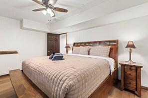 Ein Schlafzimmer mit einem Bett, einem Nachttisch, einer Lampe, einem Deckenventilator und einer Tür.