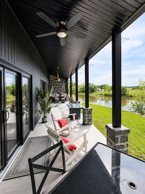 A covered outdoor patio with seating, a table, and a view of a lake.