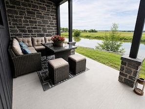 A covered patio with wicker furniture, a table with a flower arrangement, and a view of a lake.