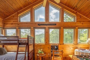 A cabin with a bunk bed, a desk with a lamp, and multiple windows offering views of the outdoors. - Hunter Jacks: Hot Tub, Mnt Views, Foosball (Sevierville)