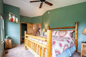Ein Schlafzimmer mit einem hölzernen Bett, einem Deckenventilator, einer grünen Wand und einer Tür zu einem weiteren Raum.