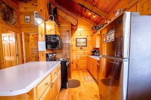 Ein Holzblockhaus-Interieur mit einer Küche, die einen Kühlschrank, einen Herd und Holzschränke enthält.