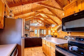 A log cabin interior with a kitchen featuring a refrigerator, stove, microwave, and wooden cabinets. - Hunter Jacks: Hot Tub, Mnt Views, Foosball (Sevierville)