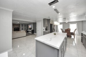 Een ruime keuken met een groot eiland, moderne apparaten en een eetgedeelte met een houten tafel en stoelen.