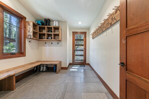 Un couloir avec un banc en bois, un porte-chaussures et une porte dotée d’un panneau de verre.
