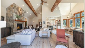 A spacious living area with a stone fireplace, wooden beams, a large sofa, and a dining area with a view.