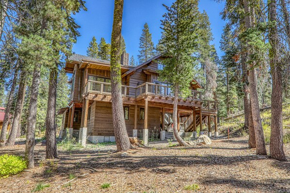 A log cabin with a balcony, surrounded by tall trees.