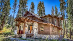A log cabin with a stone foundation, wooden exterior, and a porch with steps leading to the entrance.