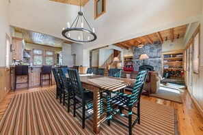 Une salle à manger spacieuse avec une grande table et des chaises en bois, un lustre et une cheminée en pierre.