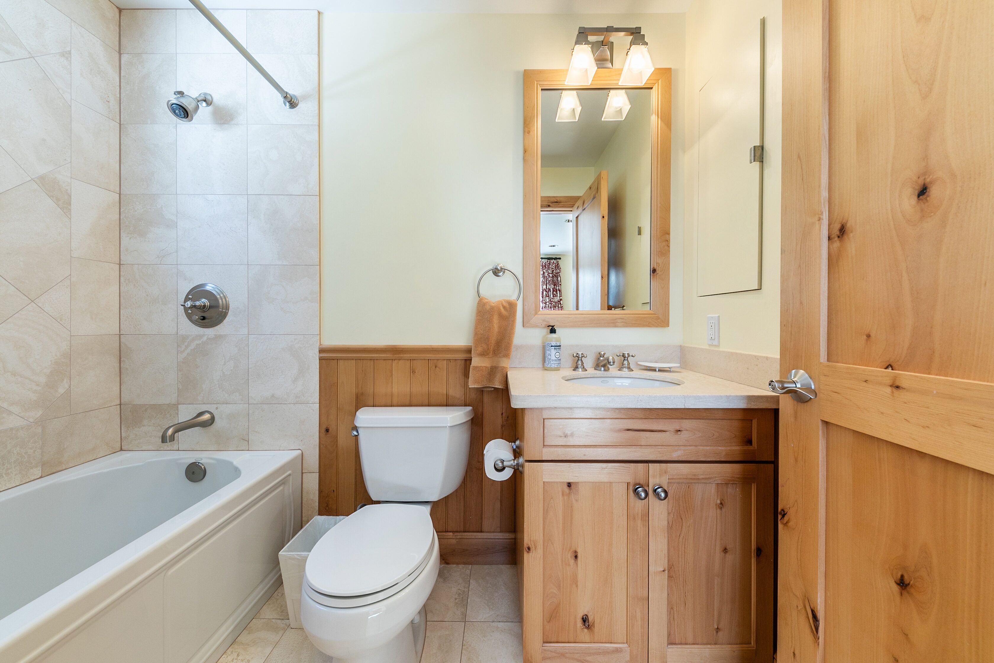 A bathroom with a bathtub, toilet, wooden vanity, and a mirror.