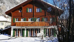 Een houten chalet met veel ramen en een balkon, omgeven door sneeuw en bergen.