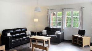 Een woonkamer met een zwarte leren bank, een houten salontafel, een tv-meubel en een vloerlamp.