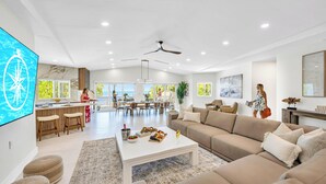 A spacious living area with a large sofa, a coffee table with snacks, a kitchen area, and a view of the outdoors.