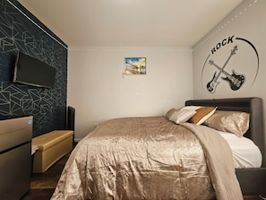 Une chambre à coucher comprenant un lit, une commode, un téléviseur et un mur orné d’une fresque sur le thème de la musique rock.
