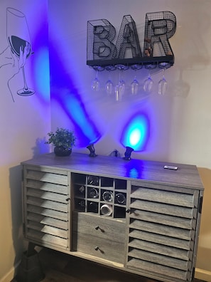 Un espace bar avec un meuble en bois, des verres à vin et une enseigne indiquant « BAR ».