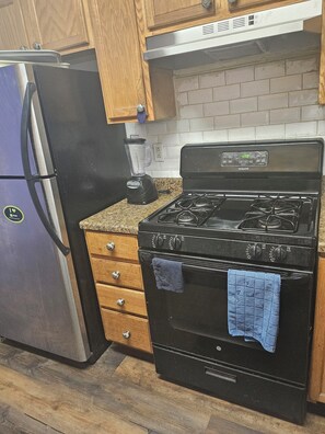 A kitchen with a stainless steel refrigerator, a black stove with a digital clock, wooden cabinets, and a granite countertop. - Enjoy this catchy, luxurious, cozy, peaceful, stylish and well decorated space (Newark)