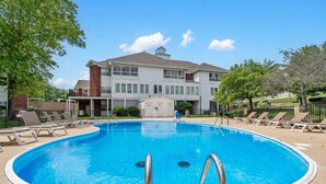 Una piscina con lettini, un edificio con un garage e cielo sereno.