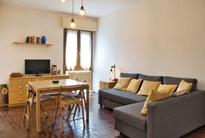 Una sala de estar moderna con un sofá, una mesa de comedor, sillas, un televisor y una estantería.