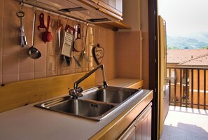 Una cocina con un lavamanos de acero inoxidable, utensilios colgantes y vistas a un balcón con tejado de baldosas.