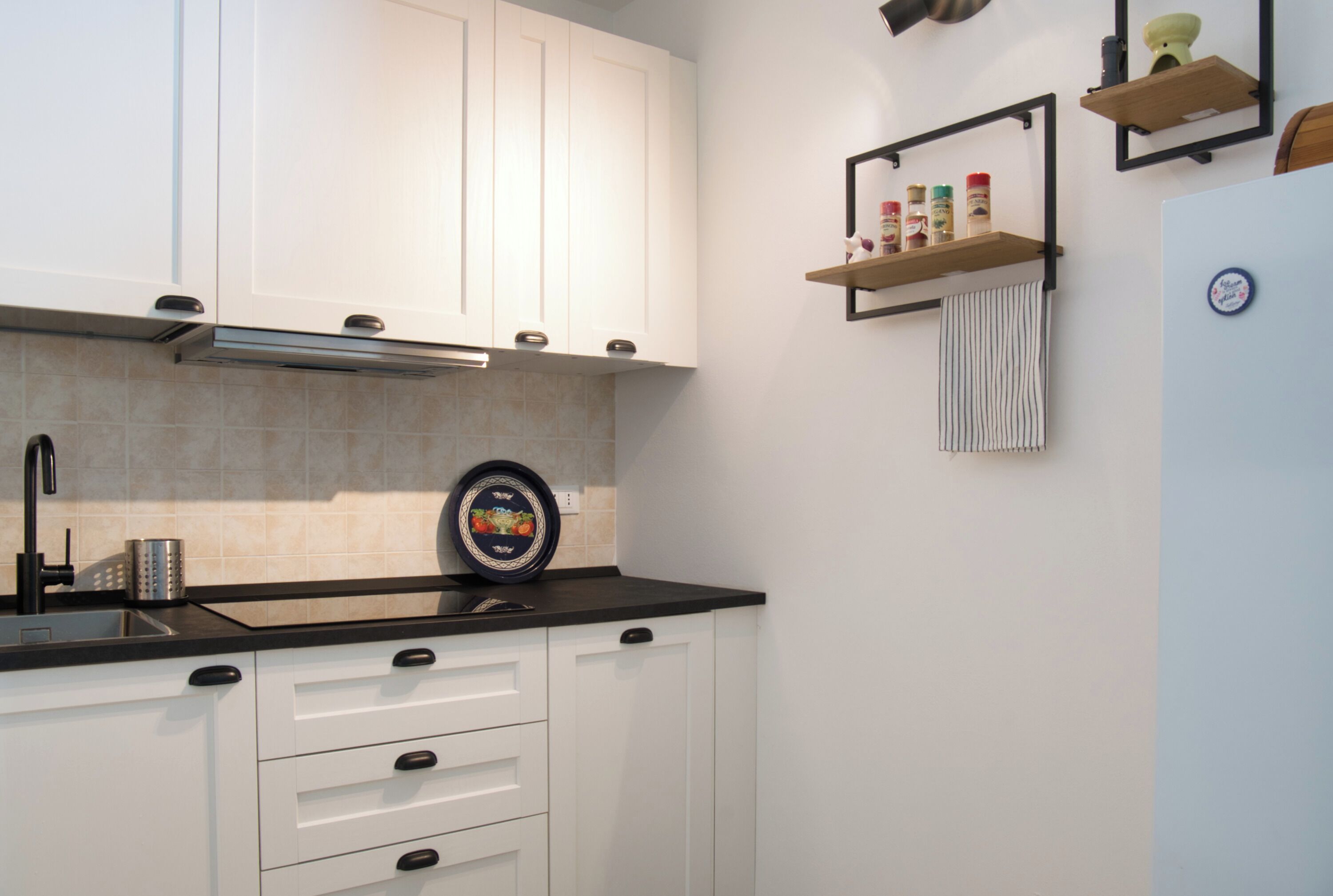 A kitchen with white cabinets, a black countertop, a stainless steel sink, and a refrigerator.