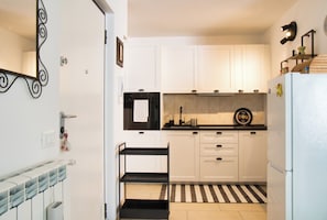 Una cocina con armarios blancos, encimera negra, alfombra a rayas y una estantería negra.
