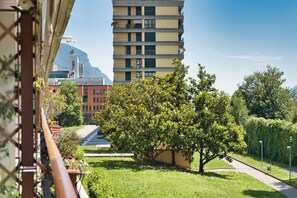 A multi-story building with balconies, a grassy area with a tree, and a clear sky. - Green Terrace Apartment in Lecco Center (Lecco)