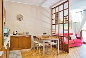 Una cocina compacta con comedor, un sofá rojo y un biombo decorativo.