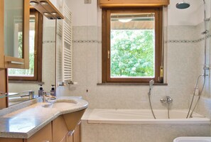 Een badkamer met een bad, een wastafel, een raam en een douche.