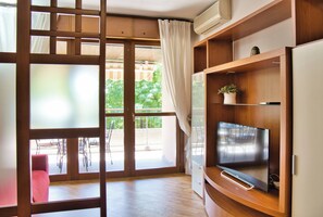 A modern living room with a flat-screen TV, wooden shelving, and a sliding glass door leading to an outdoor patio. - Green Terrace Apartment in Lecco Center (Lecco)