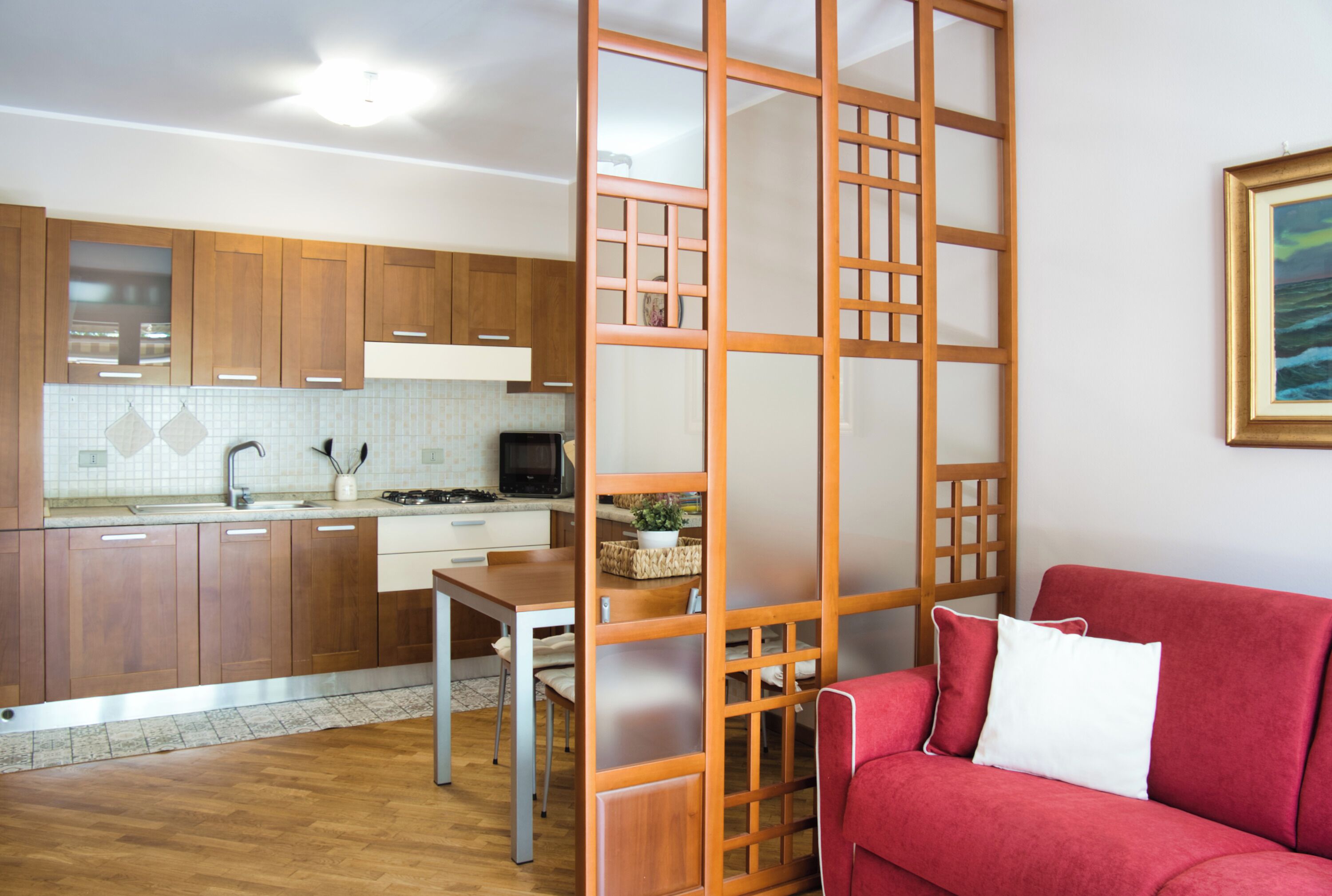 Een moderne keuken met houten kastjes, een eettafel en een rode bank in een woonruimte.
