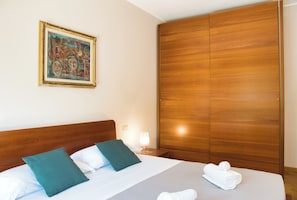 Ein Hotelzimmer mit einem hölzernen Kopfteil, einem Bild an der Wand, einem Bett mit grün-weißen Kissen und einem Holzschrank.