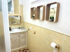 Casa de banho com lavatório, espelho, sanita e rolo de papel higiénico.