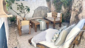 En udendørs terrasse med et træbord, to stole, en sofa og en stor klippevæg.