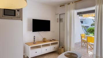 Una habitación con televisión montada en la pared, un aparador de madera con cajones, una mesita y una cesta de mimbre.