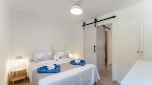 Habitación de hotel con cama, mesita de noche con lámpara, puerta corredera y pared blanca.