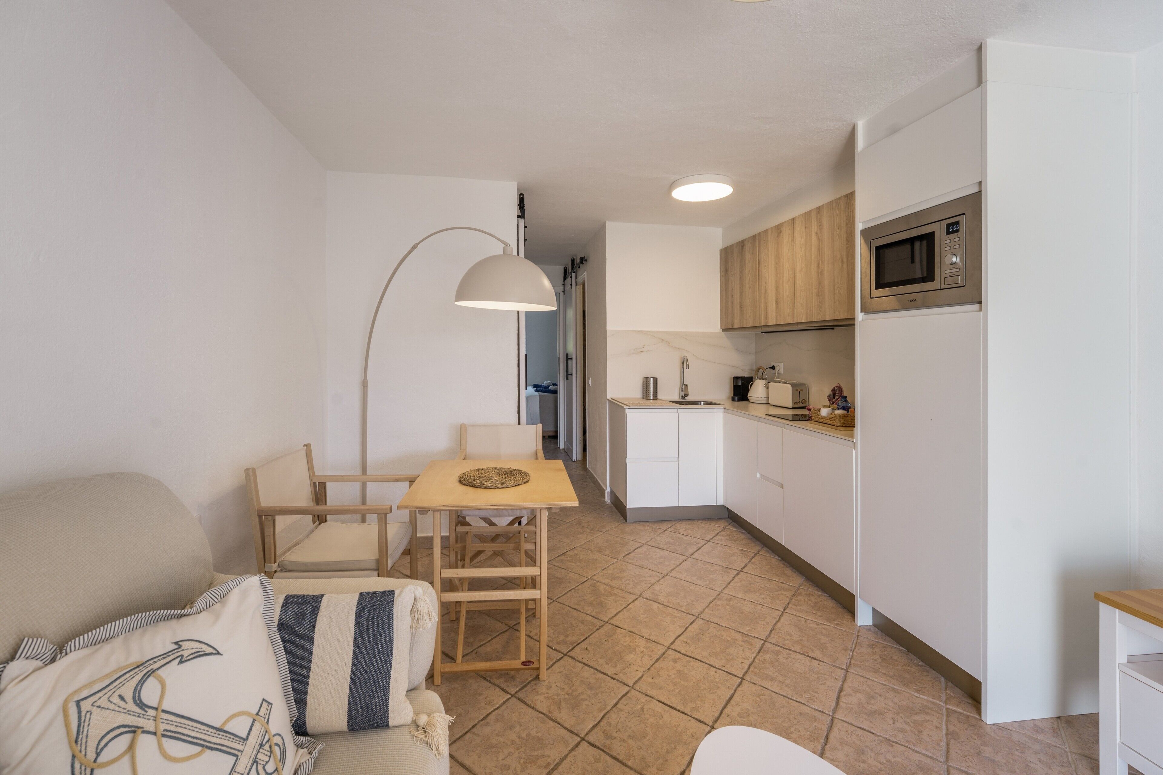 Un espacio habitable compacto con kitchenette, una zona de comedor con mesa y sillas, y un sofá.