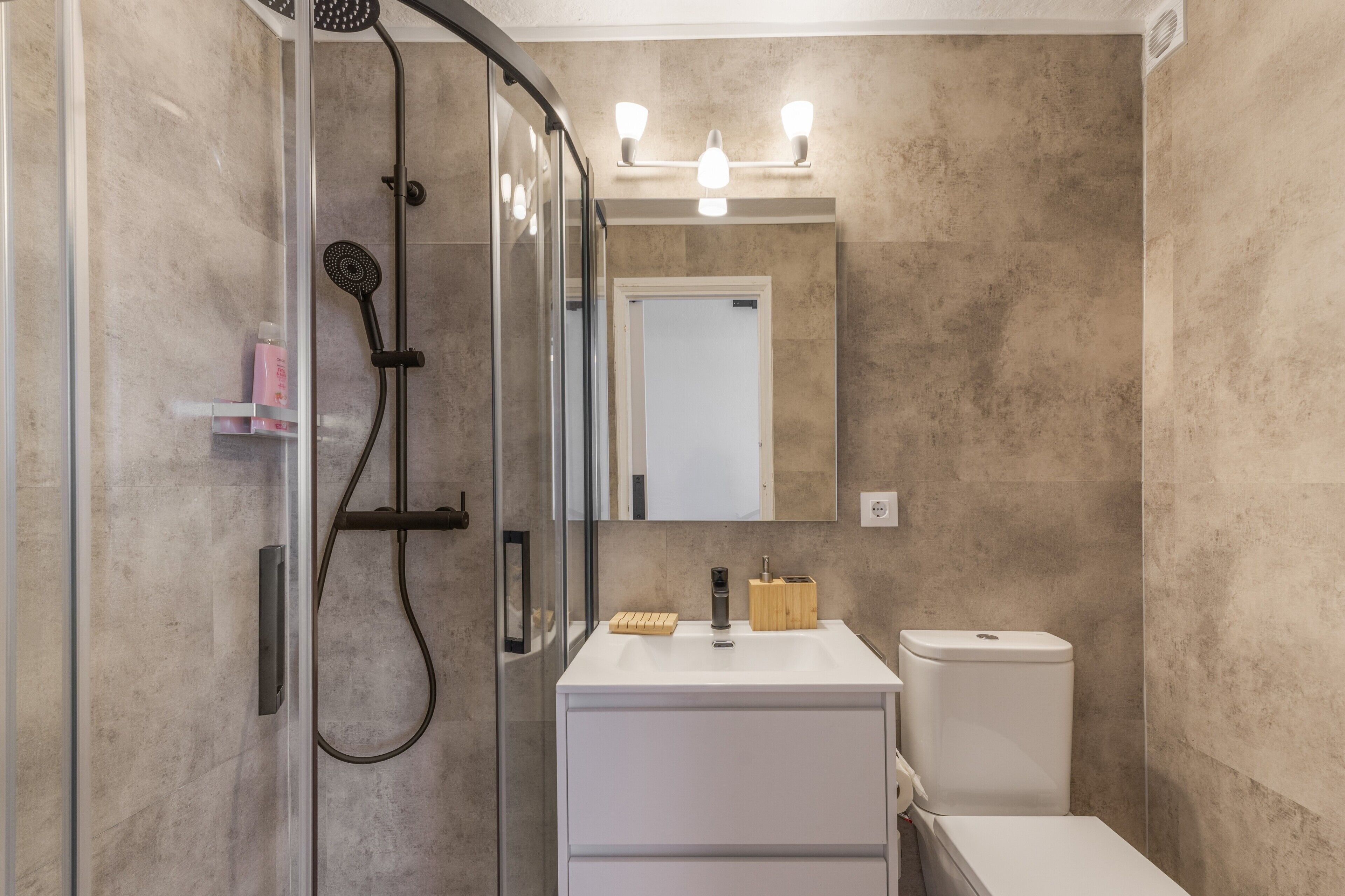 A modern bathroom with a glass shower enclosure, a white sink, and a mirror above it.