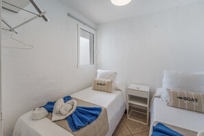 A hotel room with two beds, a small bedside table, a window, and a wall-mounted towel rack.