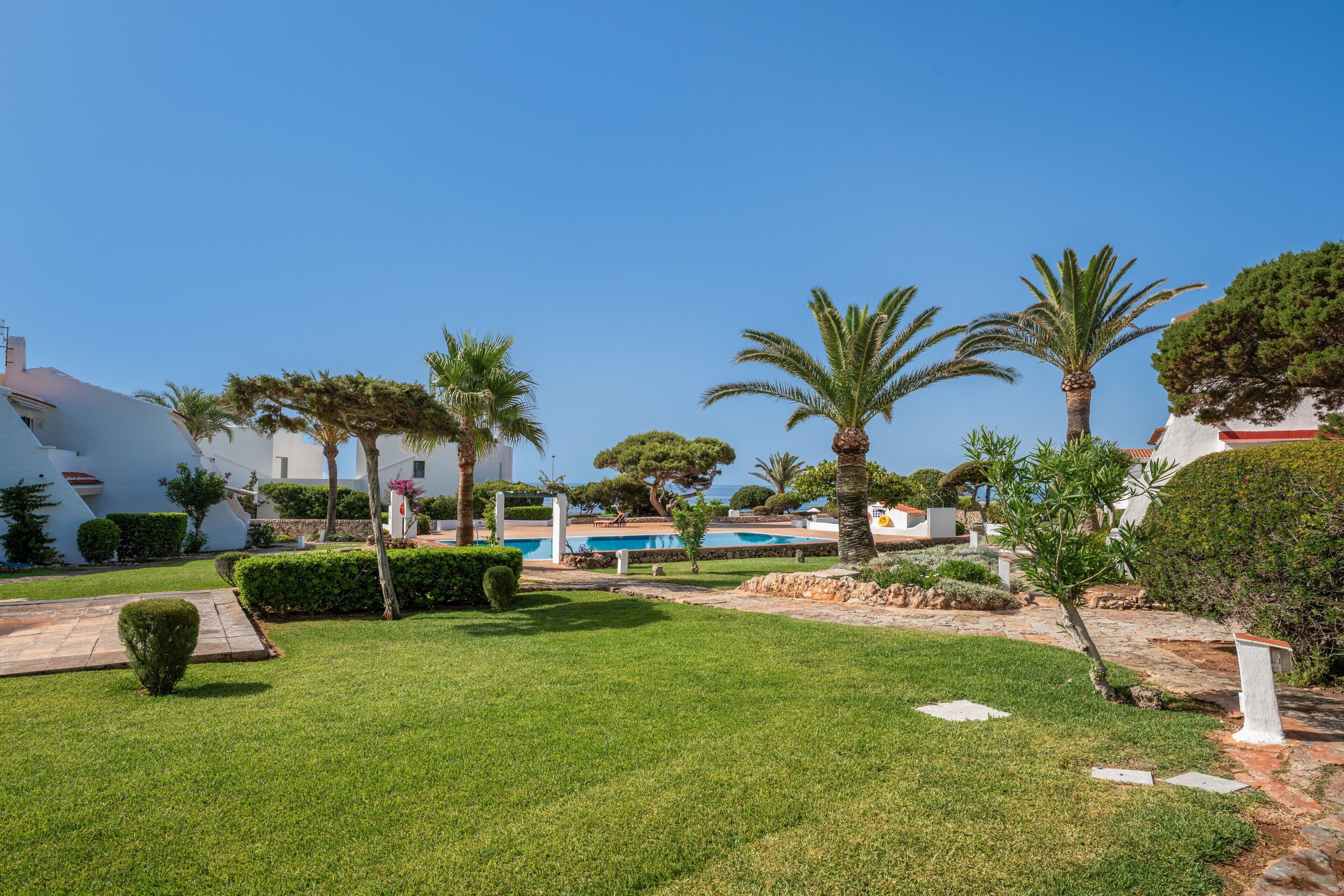 Un jardin bien entretenu, agrémenté d’une piscine, de palmiers et de haies soigneusement taillées.