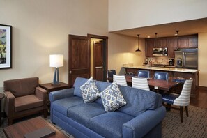 A living room with a sofa, a coffee table, a lamp, and a dining area with chairs and a table. - Cozy 2-bedroom in Canyons Village, Park City, Utah. Walking distance to lifts. (Park City)