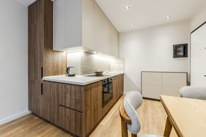 A modern kitchen with wooden cabinets, a built-in oven, and a dining area with a wooden table and chairs. - Metropolitan Living 1BR City Apartment (Tirana)