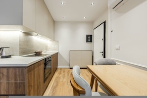A modern kitchen with wooden cabinets, a built-in oven, and a dining area with a wooden table and chairs. - Metropolitan Living 1BR City Apartment (Tirana)