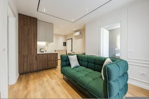 A modern living room with a green sofa, wooden cabinets, and a kitchen area in the background. - Metropolitan Living 1BR City Apartment (Tirana)