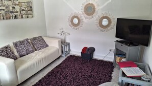 A living room with a white sofa, a dark purple rug, a TV, and wall art. - Bungalow - Sleeps 4 - Parking - Garden (Nottingham)