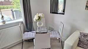 A modern room with a glass table, white chairs, a white sofa, and a window with curtains. - Bungalow - Sleeps 4 - Parking - Garden (Nottingham)