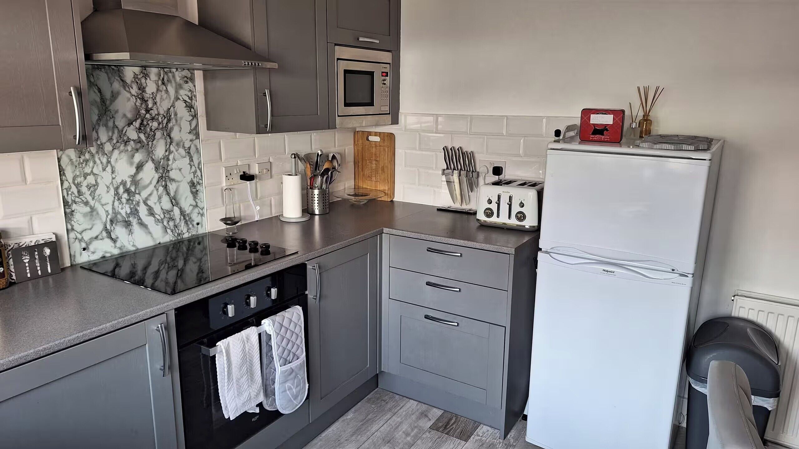 Une cuisine moderne avec des meubles gris, une cuisinière noire, un four à micro-ondes, un grille-pain et un réfrigérateur.