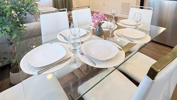 A modern dining area with a glass table, white chairs, and a chandelier.