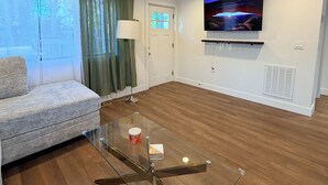 A modern living room with a glass coffee table, a sofa, a TV mounted on the wall, and a door with a window.