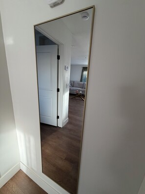 En gang med et stort spejl, der reflekterer et rum med en d ør, en lyskontakt og en stikkontakt på væggen.